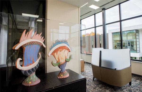 Two small, colorful sculptures sit on a table next to a window.